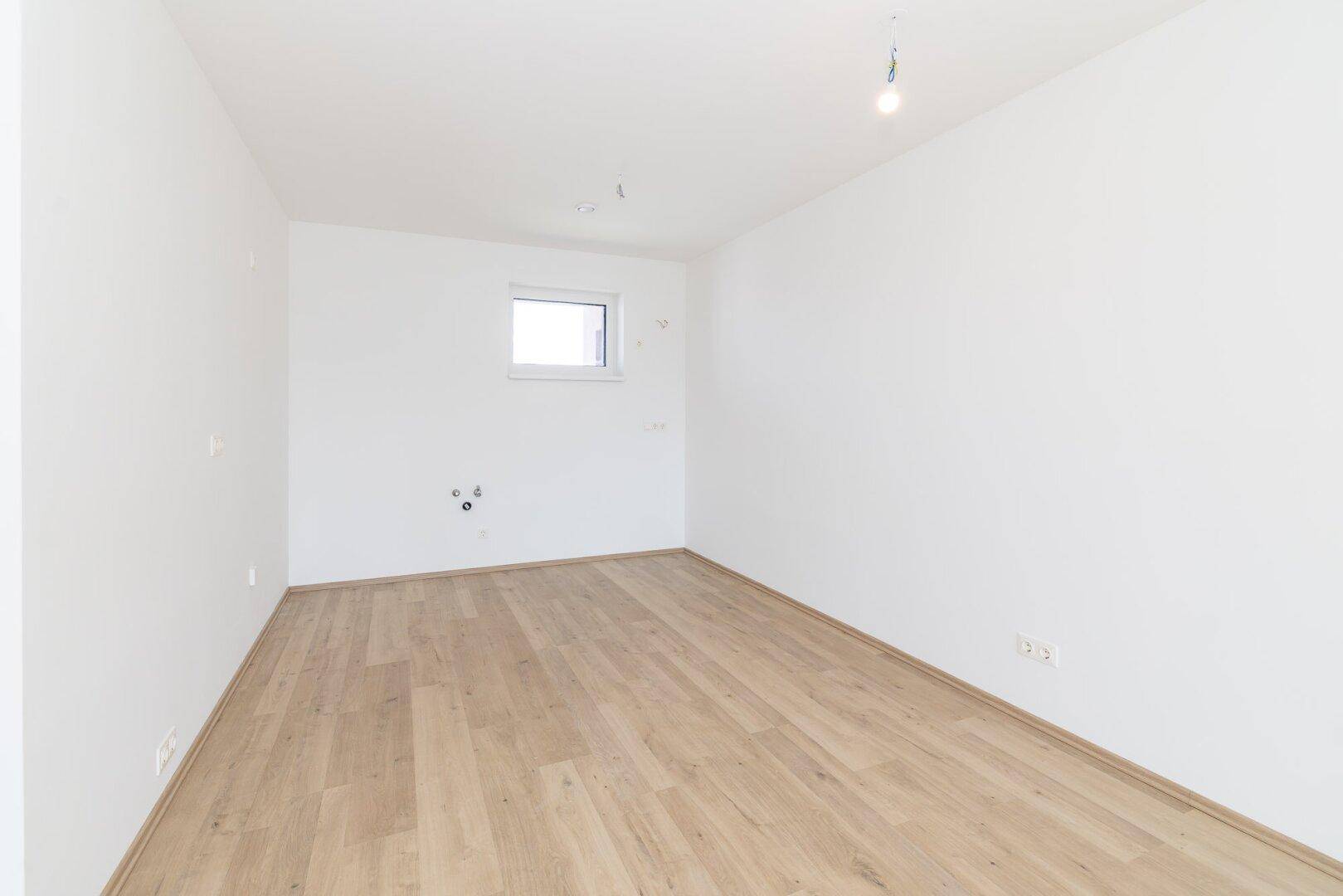 Leerer Raum mit hellem Laminatboden und weißen Wänden, vorbereitet für eine Kücheninstallation.
