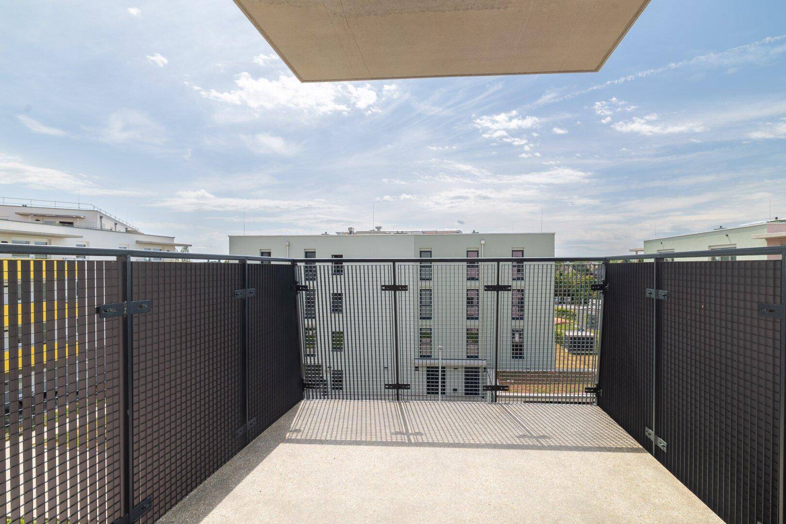 Geräumige Terrasse mit Betonboden und Metallgeländer, umgeben von modernen Wohngebäuden.