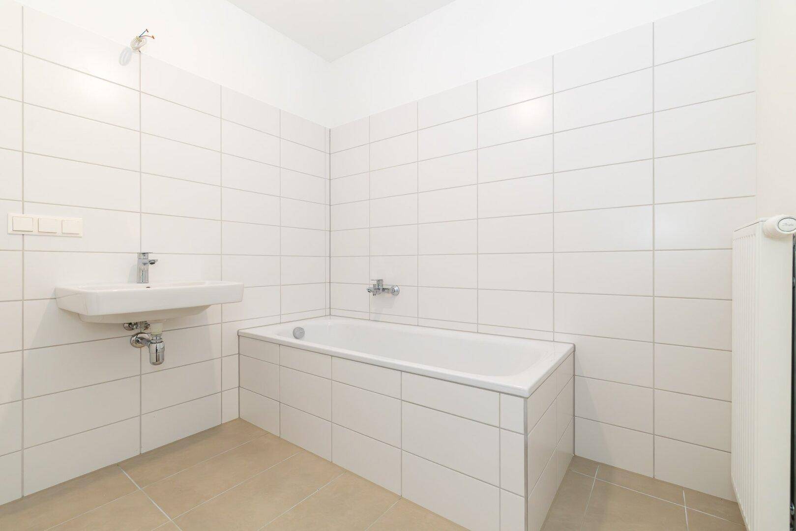 Helles Badezimmer mit beigefarbenen Fliesen, weiß gefliesten Wänden und einer Badewanne.