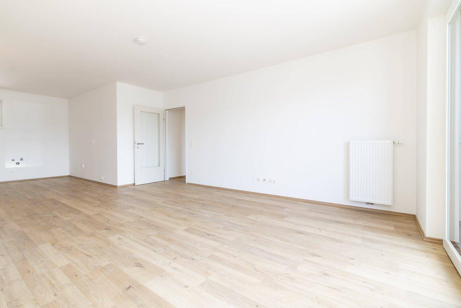 Heller, leerer Raum mit hellem Laminatboden und weißen Wänden, bereit zur individuellen Gestaltung.
