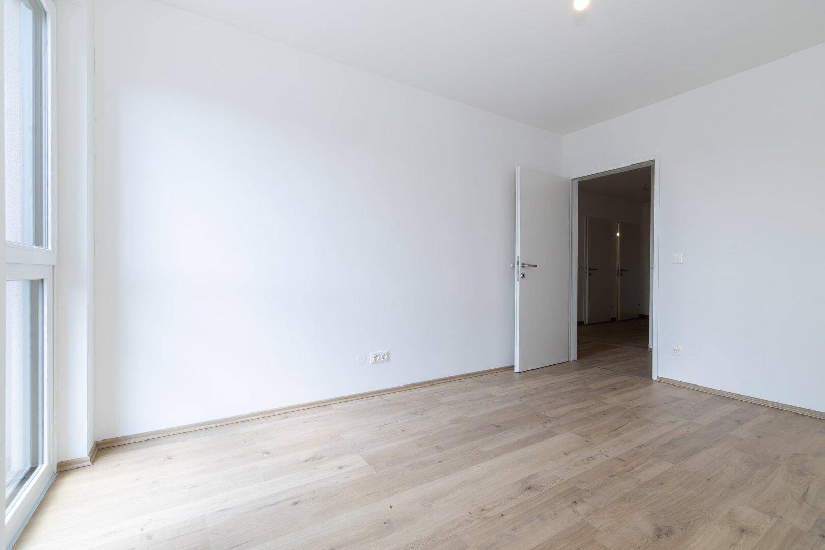 Heller Raum mit Laminatboden und offenem Zugang zu weiteren Wohnbereichen, ideal für flexible Nutzung.
