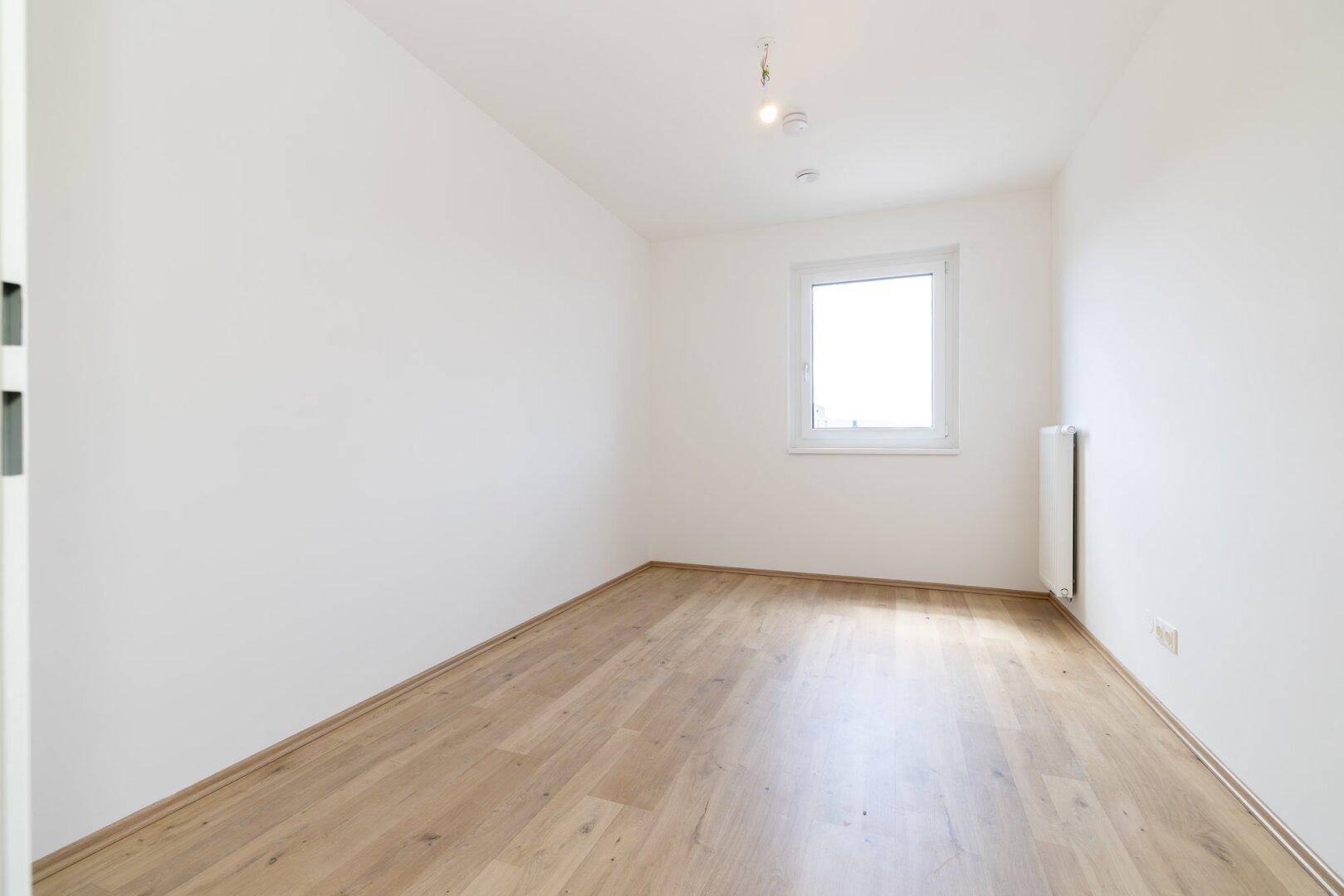Gemütliches Zimmer mit Laminatboden und einem Fenster, ideal als Kinder- oder Gästezimmer in neuem Zustand.