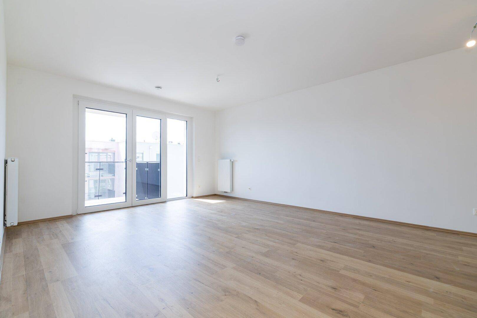 Geräumiger, heller Wohnraum mit großen Fenstern und Zugang zu einem Außenbereich, ideal für modernes Wohnen.