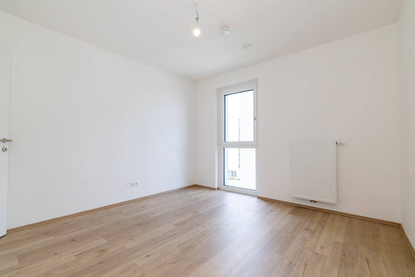 Helles Zimmer mit Laminatboden und Fenster, geeignet als Schlaf- oder Arbeitszimmer.