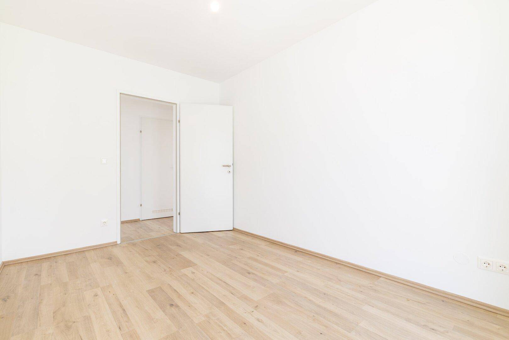 Leeres Zimmer mit Laminatboden und weiß gestrichenen Wänden, ideal als Schlafzimmer.