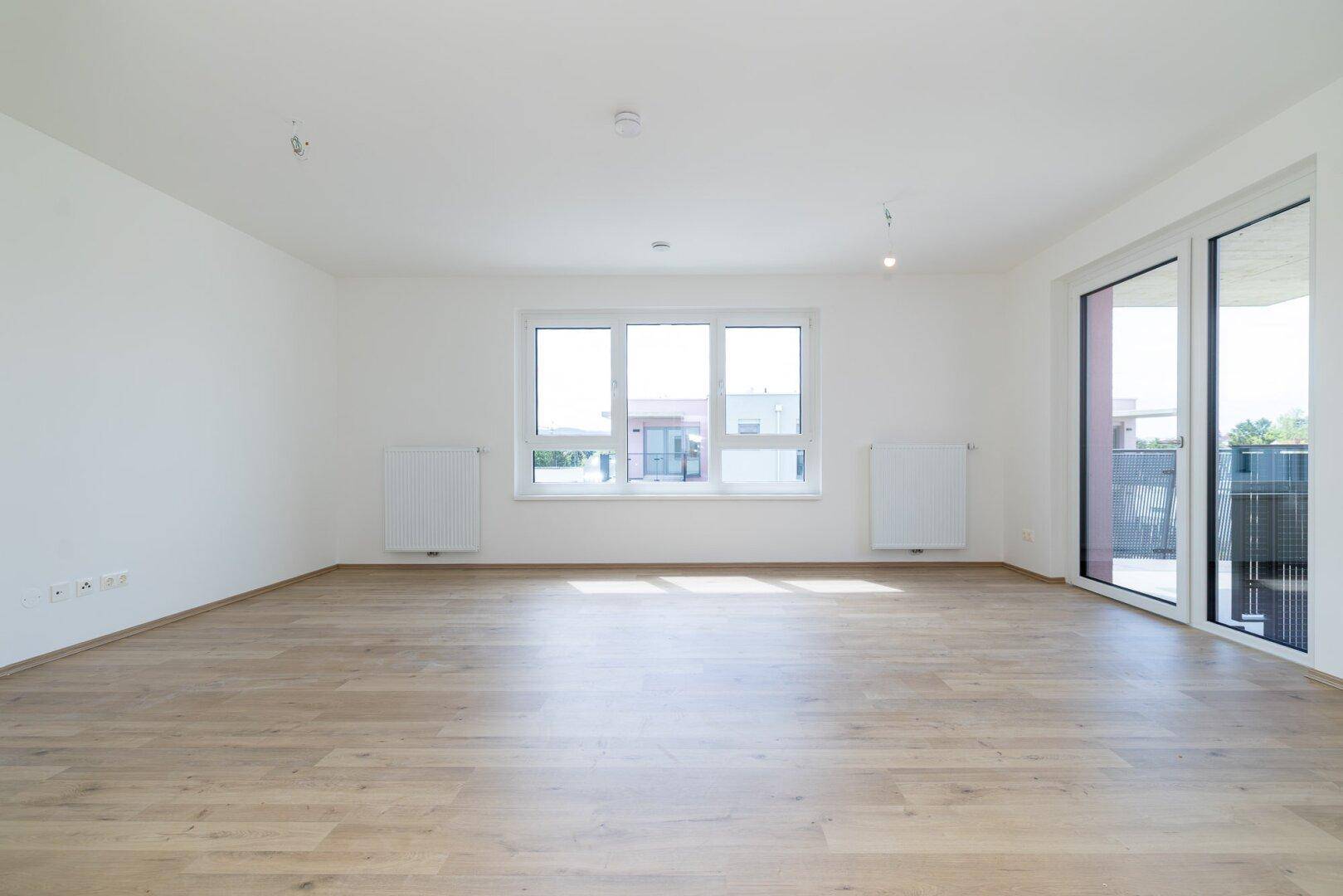 Lichtdurchfluteter Raum mit Laminatboden und breiten Fenstern, ideal für einen Wohnbereich.