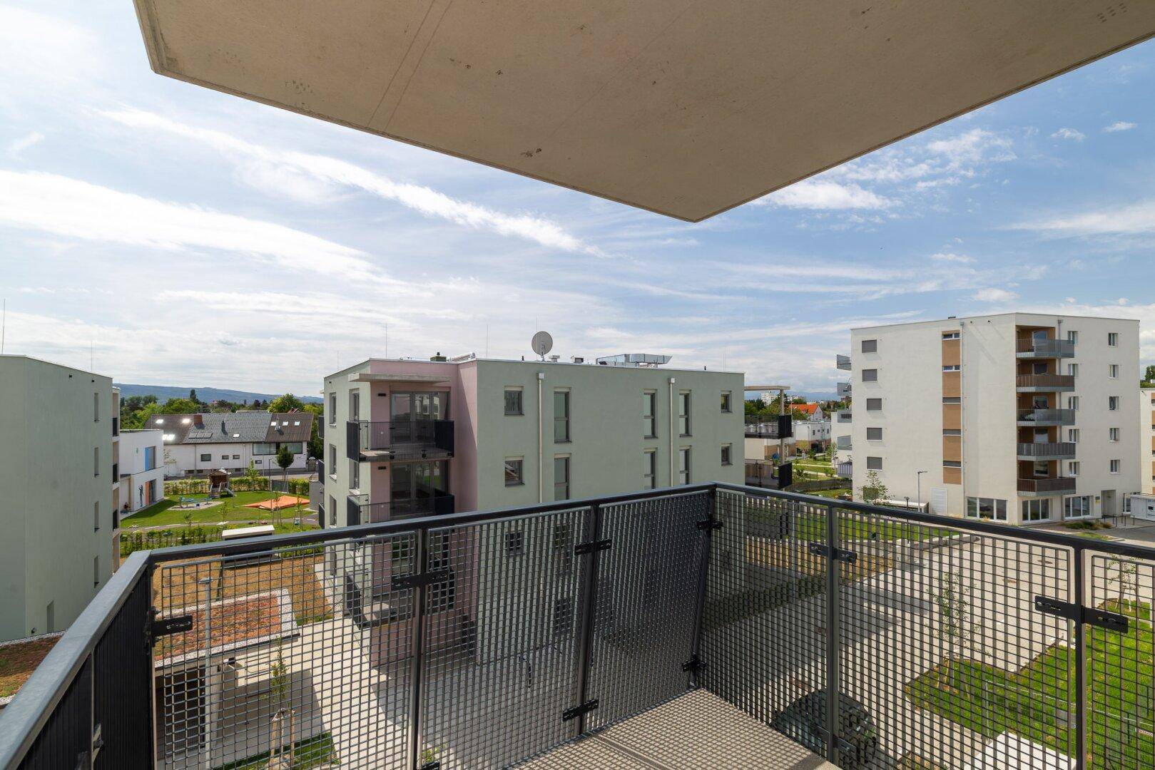 Balkon mit weitem Blick über die moderne Wohnsiedlung und einen Spielplatz, ideal für Familien.