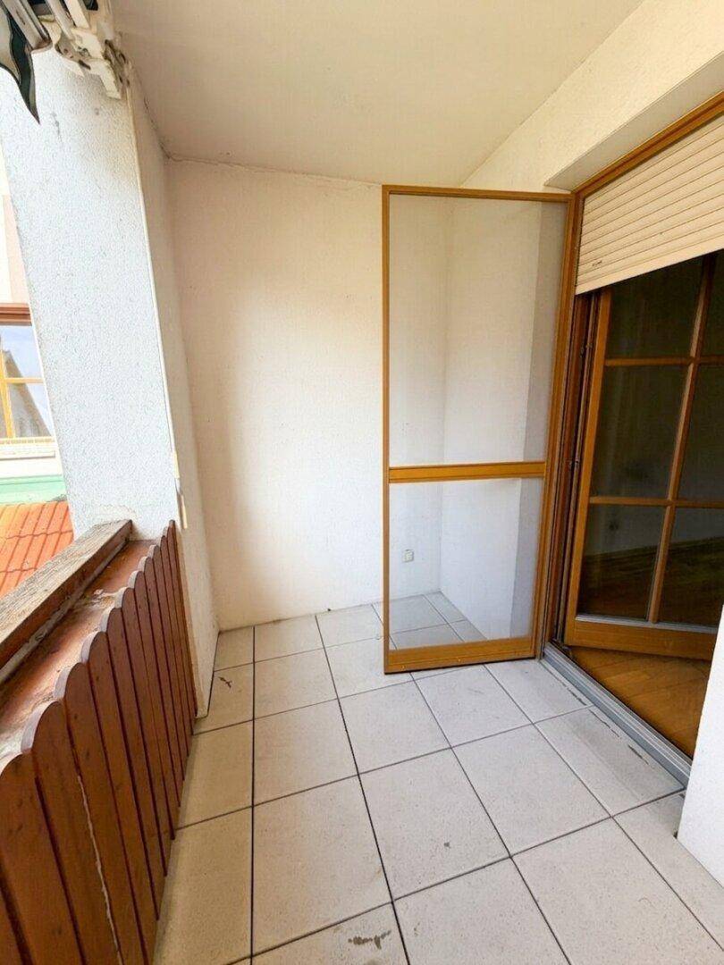 Balkon mit Fliesenboden und Holzgeländer, mit offener Insektenschutztür.