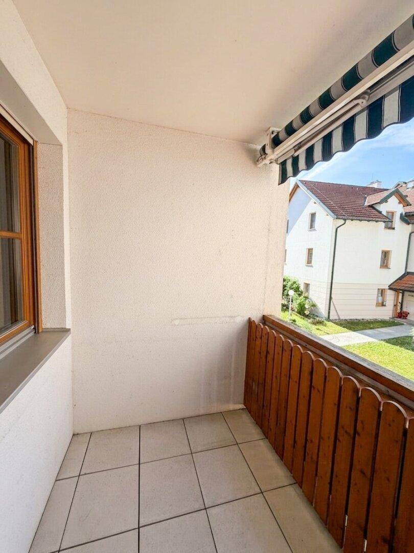 Heller Balkon mit Fliesenboden, Holzgeländer und Blick auf den grünen Innenhof.