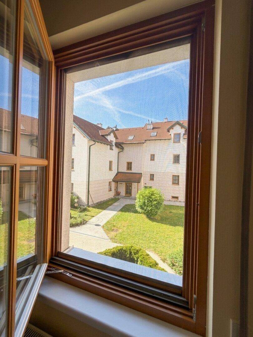 Blick aus dem Fenster auf den gepflegten grünen Innenhof und die umliegenden Gebäude.