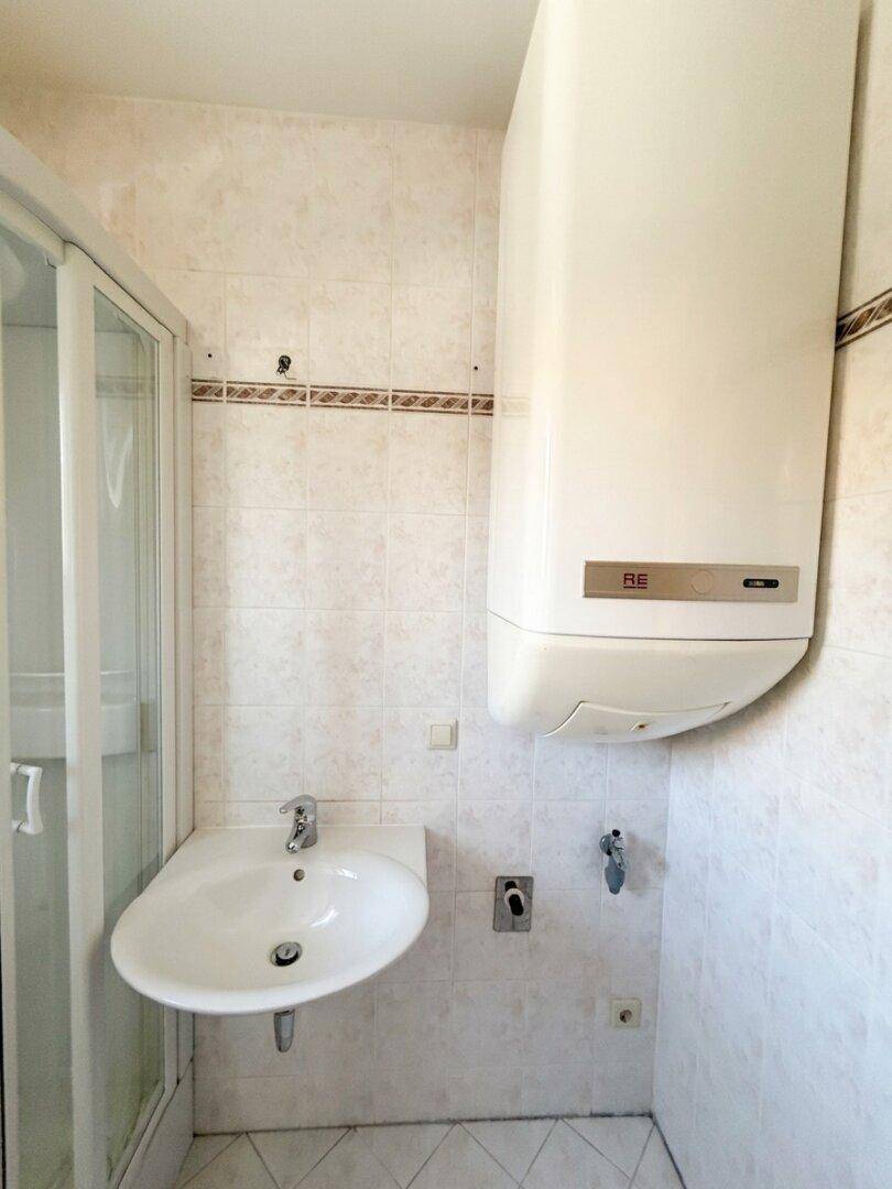 Waschbecken und Warmwasserboiler in einem gefliesten Badezimmer.