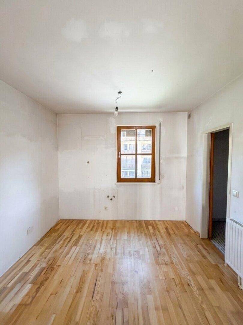 Unmöblierter Raum mit Holzboden und Fenster, bereit für individuelle Gestaltung.