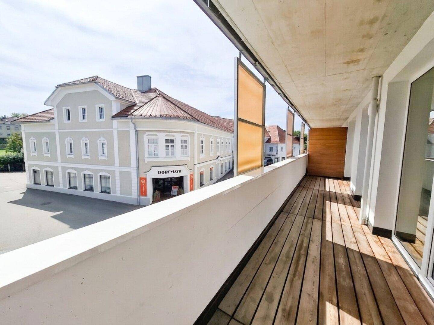 Geräumiger Balkon mit Holzdielen und Blick auf die Straße und ein historisches Gebäude.