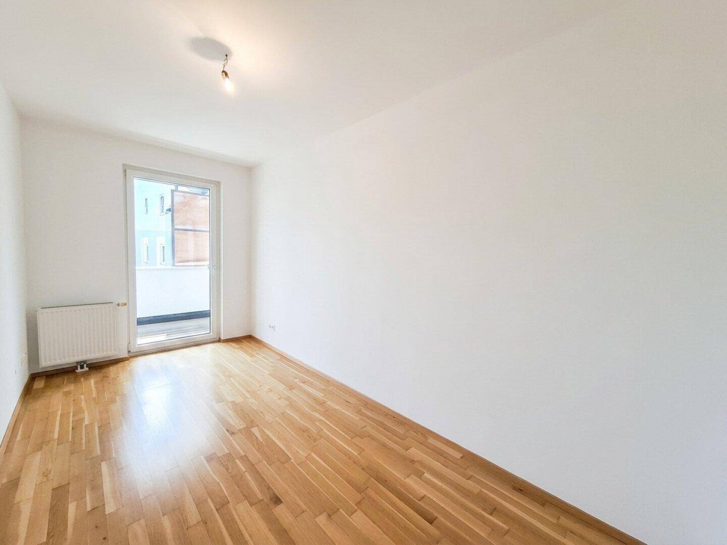 Leeres Schlafzimmer mit Parkettboden und Zugang zu einem Balkon, ideal für Ruhe.