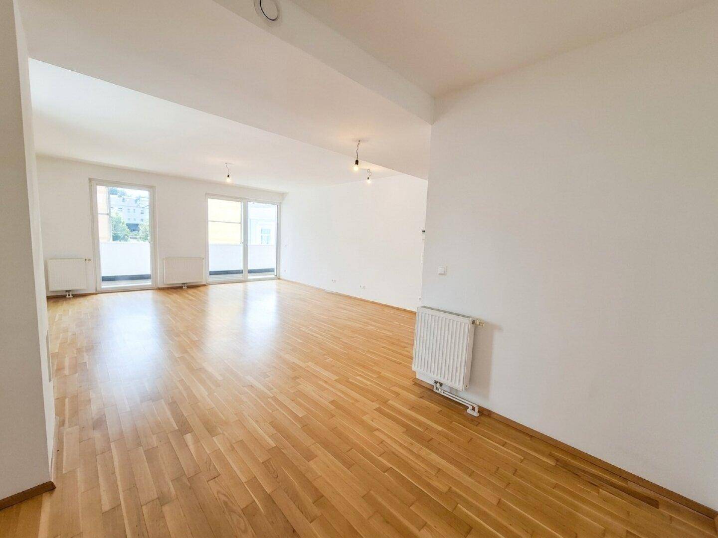 Heller Wohnbereich mit Parkettboden und Heizkörpern, der viel Platz für Möbel bietet.