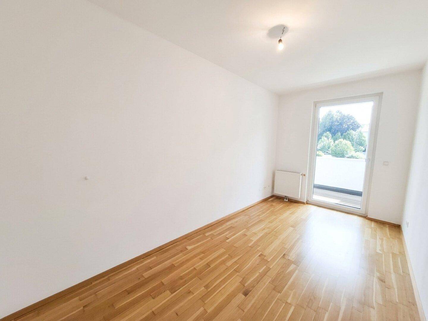 Geräumiges Schlafzimmer mit Parkettboden und Balkonzugang, bietet viel Tageslicht.