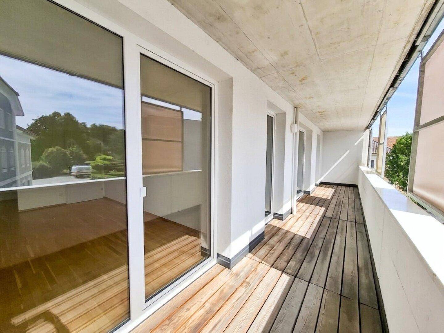 Schmaler Balkon mit Holzboden und mehreren Fenstertüren, die in die Innenräume führen.