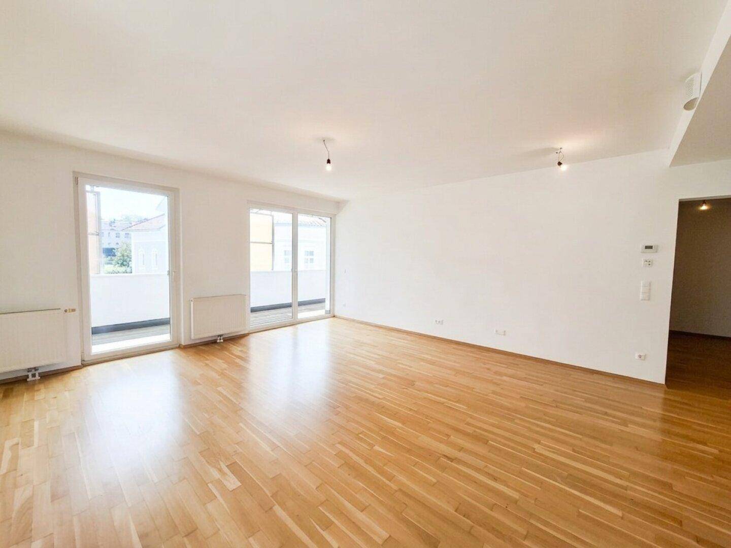 Großes, helles Wohnzimmer mit Parkettboden und zwei Zugängen zum Balkon, lichtdurchflutet.