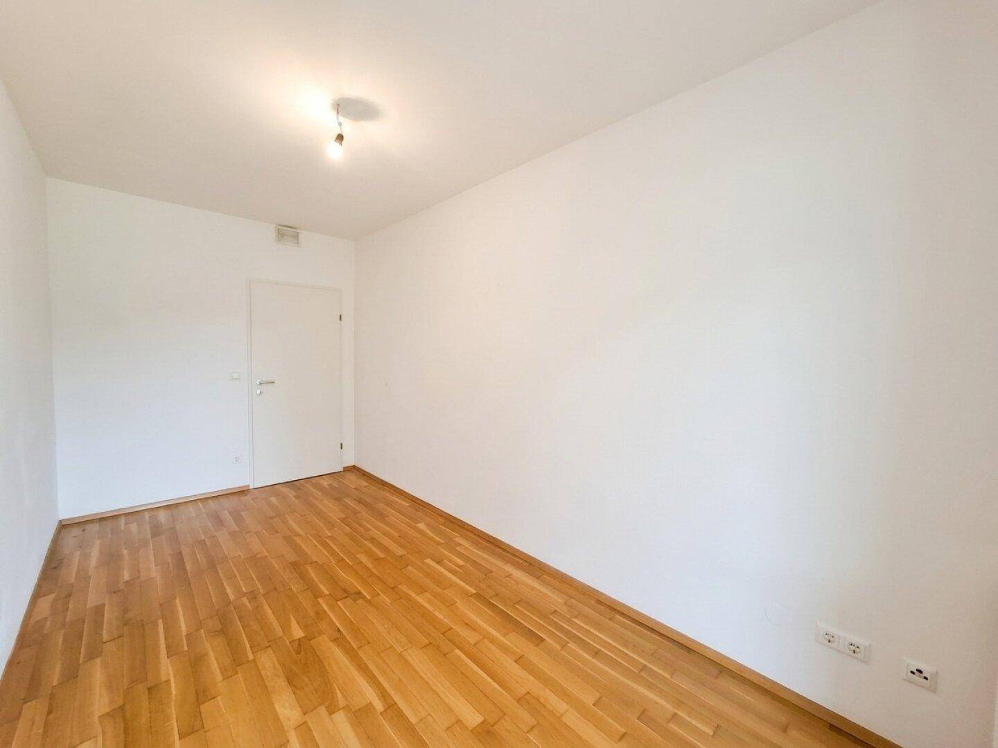 Helles Schlafzimmer mit Parkettboden und einer Tür, bereit für individuelle Gestaltung.