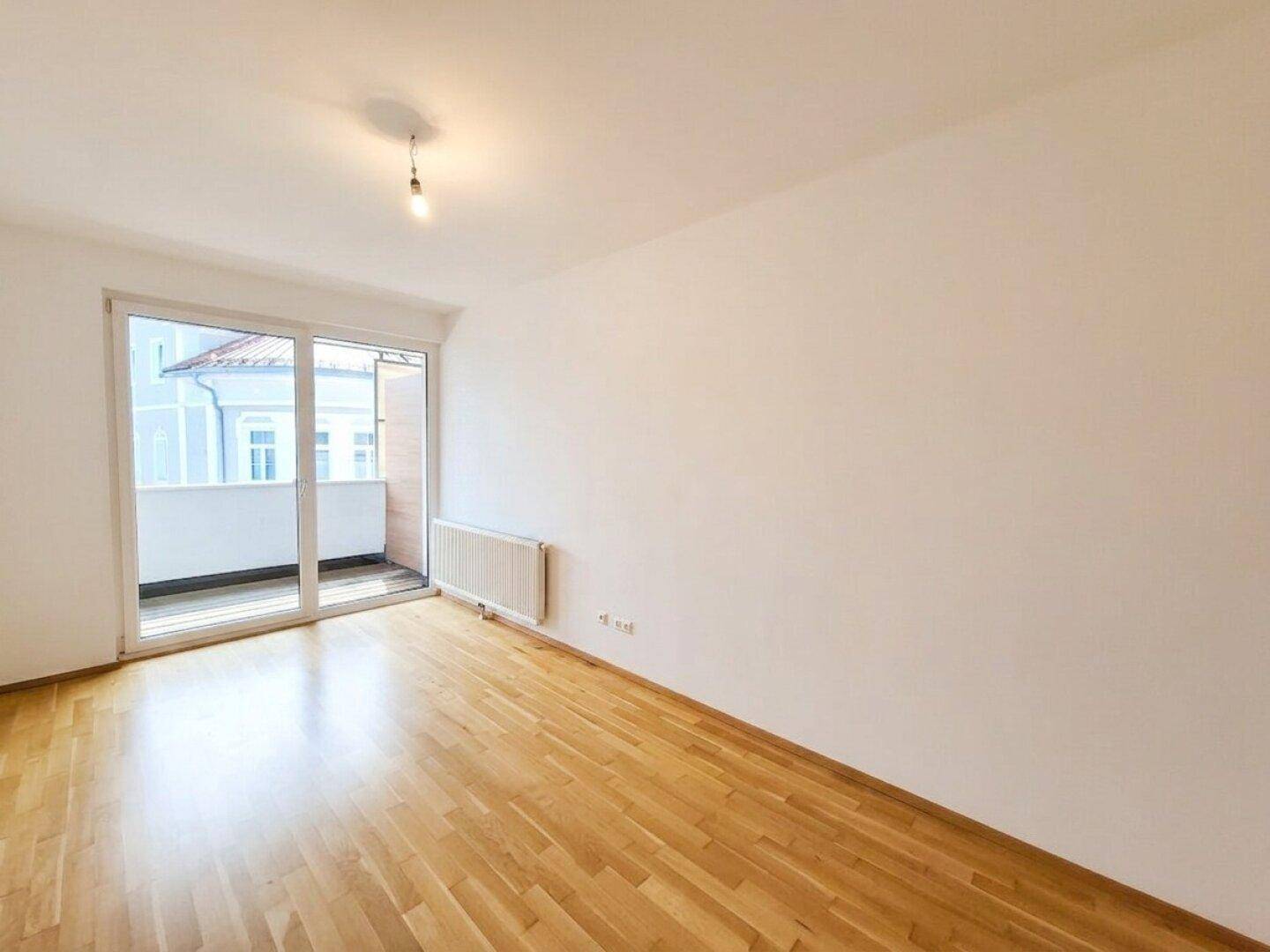 Schlafzimmer mit Parkettboden und großem Fenster, das viel Tageslicht hereinlässt.