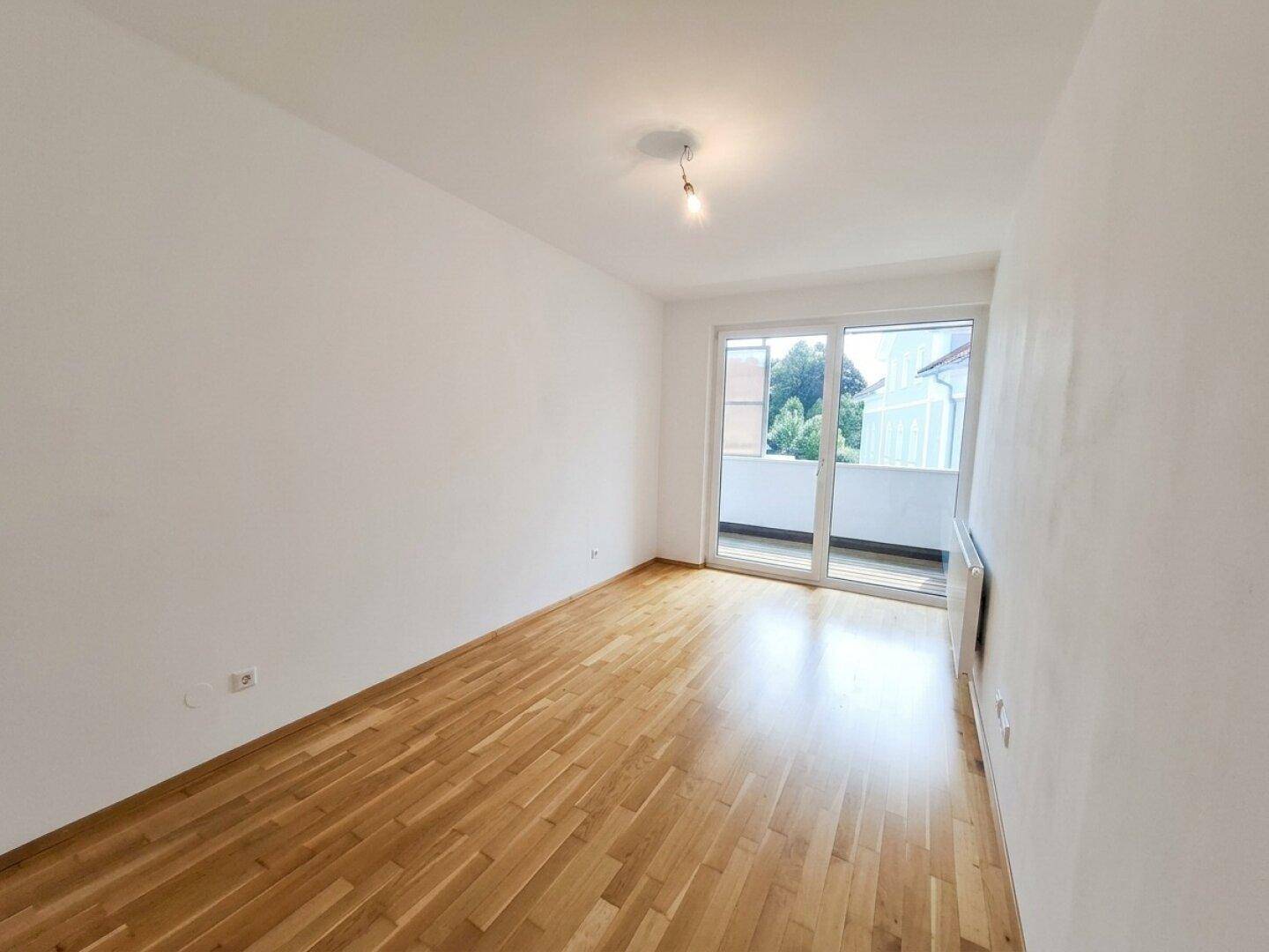 Helles Schlafzimmer mit Parkettboden und Balkonzugang, bietet eine angenehme Atmosphäre.