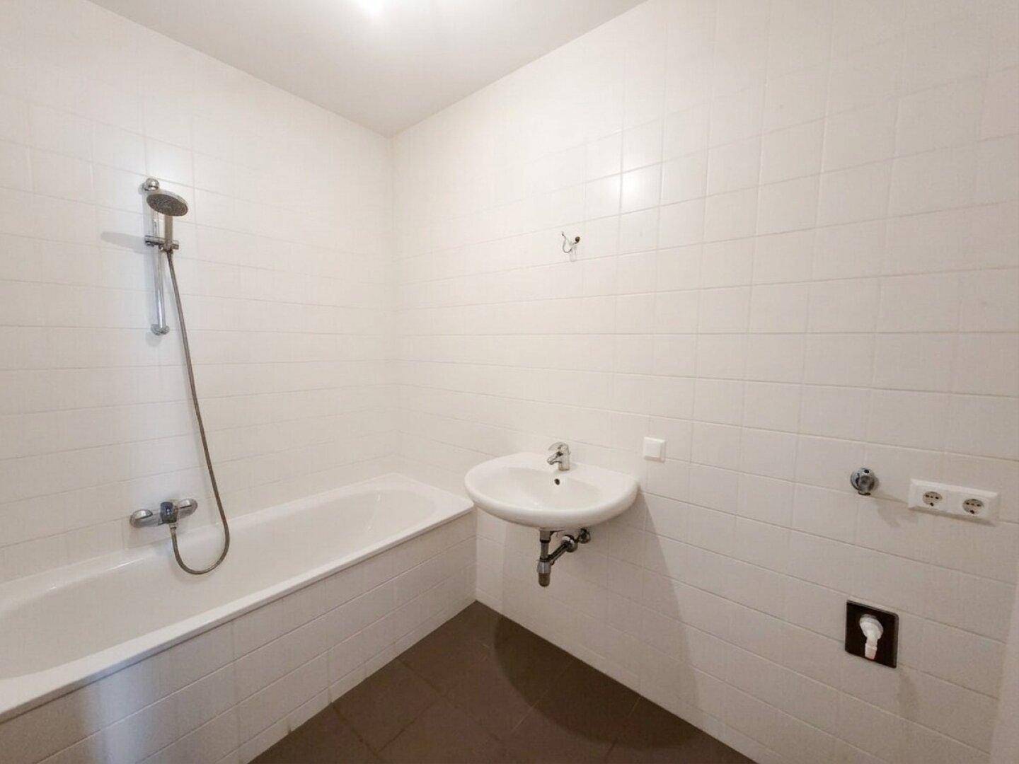 Badezimmer mit Badewanne, Dusche und Waschbecken, komplett gefliest in Weiß und Braun.