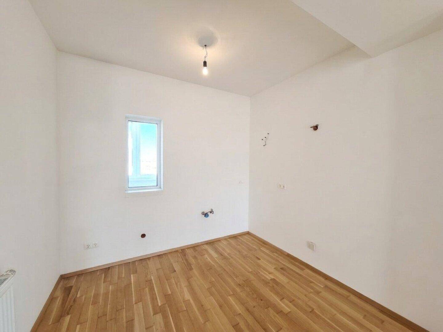 Helles Schlafzimmer mit Parkettboden und einem Fenster, bereit für neue Einrichtungsideen.