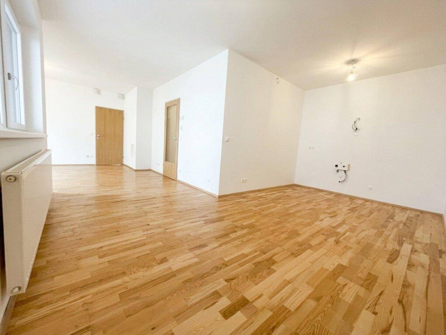 Geräumiges Wohnzimmer mit hellem Parkettboden und neutralen Wänden, ideal für moderne Einrichtung.