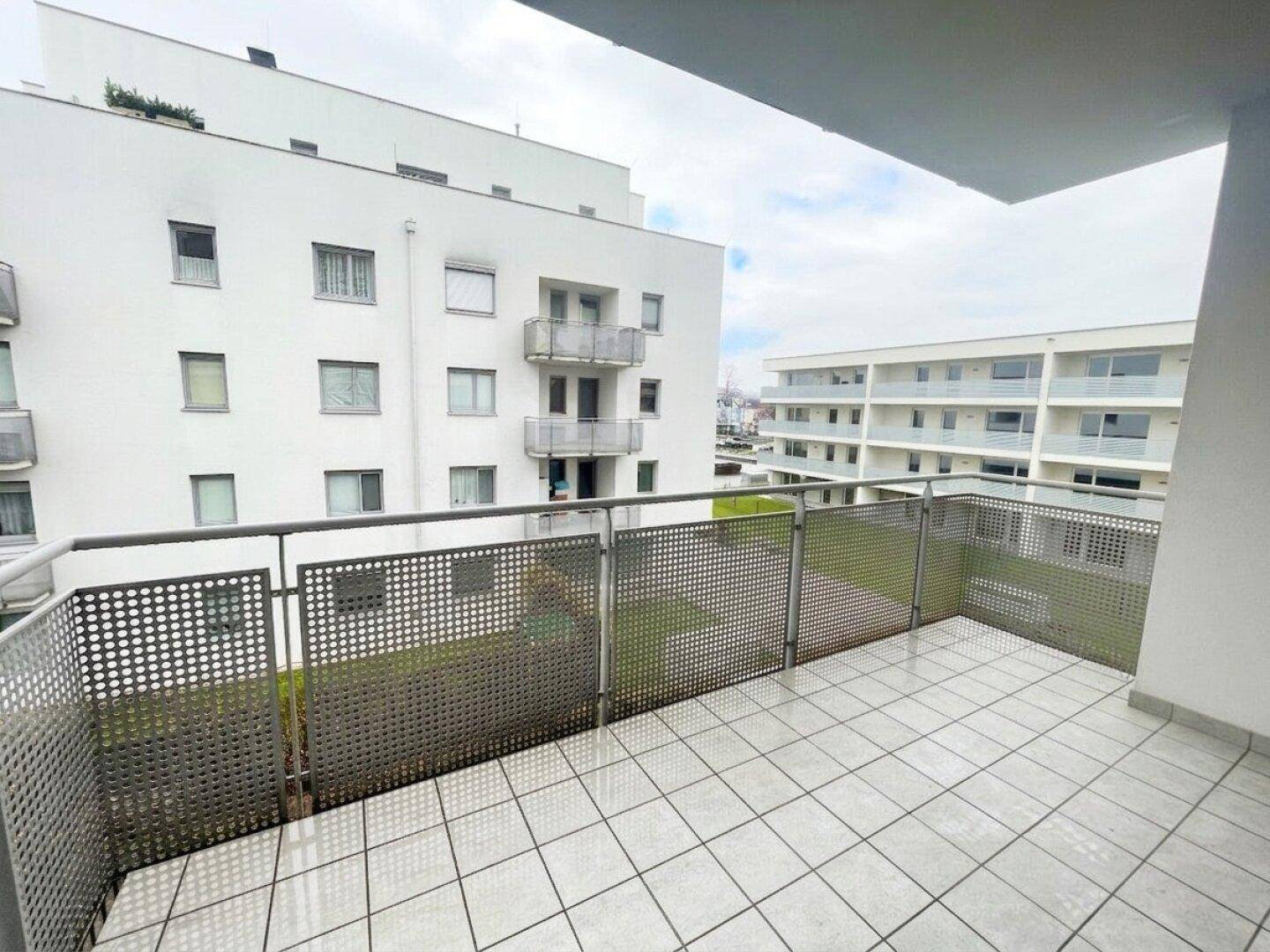 Geräumiger Balkon mit Fliesenboden und Blick auf die umliegenden Wohngebäude und Grünflächen.