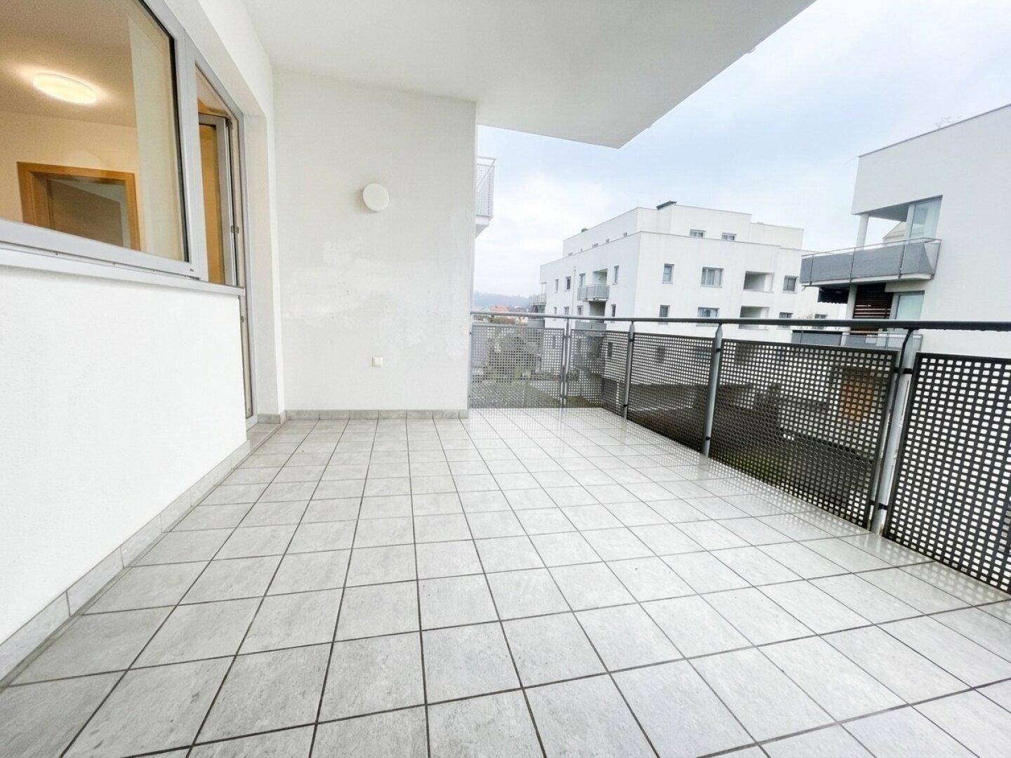 Heller Balkon mit modernen Fliesen und Metallgeländer, bietet Platz für entspannte Stunden im Freien.