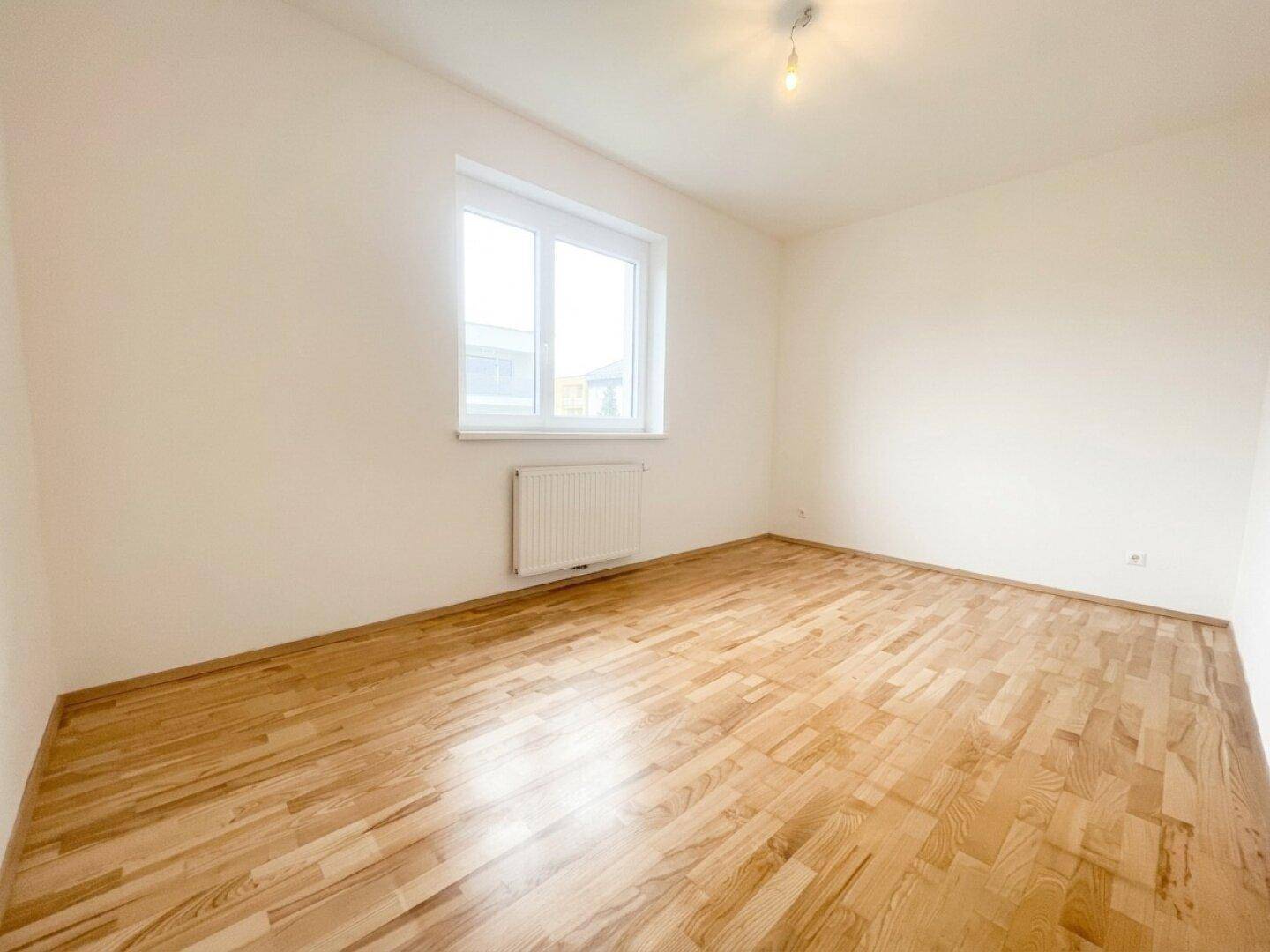 Helles Schlafzimmer mit Parkettboden und großem Fenster, bietet eine ruhige Atmosphäre.