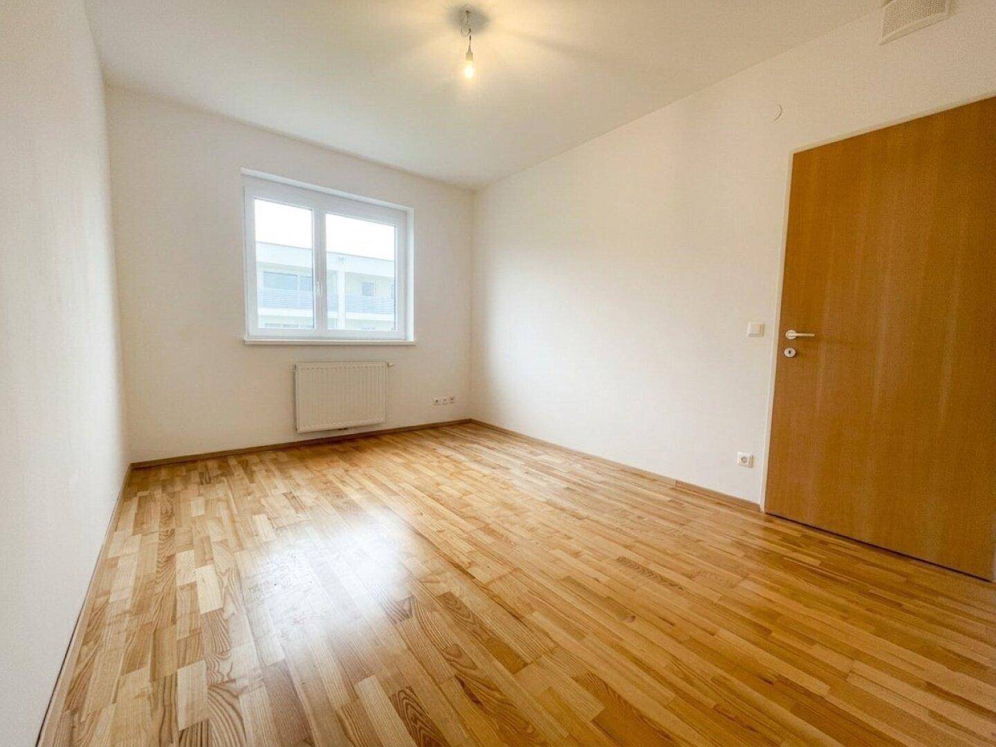 Geräumiges Schlafzimmer mit hellem Parkett und Fenster, ideal für individuelle Einrichtungswünsche.