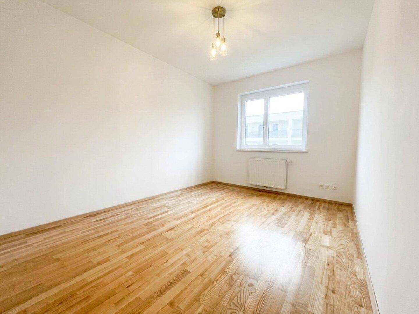 Freundliches Schlafzimmer mit Parkettboden und viel Tageslicht, ausgestattet mit einer modernen Deckenleuchte.