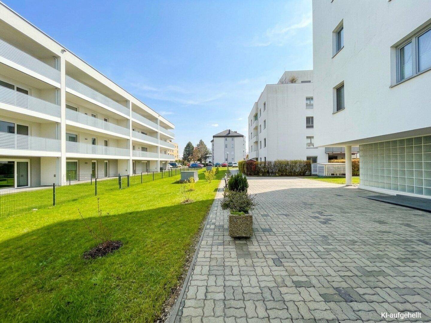 Moderne Wohnanlage mit weißen Fassaden, gepflegten Grünflächen und sonnigem Außenbereich.