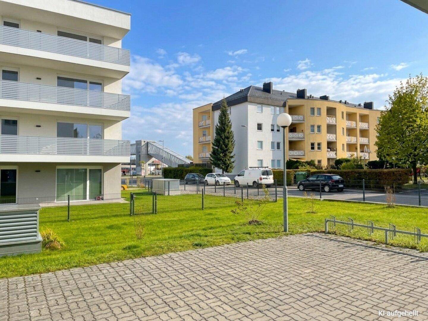 Außenansicht der Wohnanlage mit modernen Gebäuden, grünen Rasenflächen und gepflastertem Parkbereich.