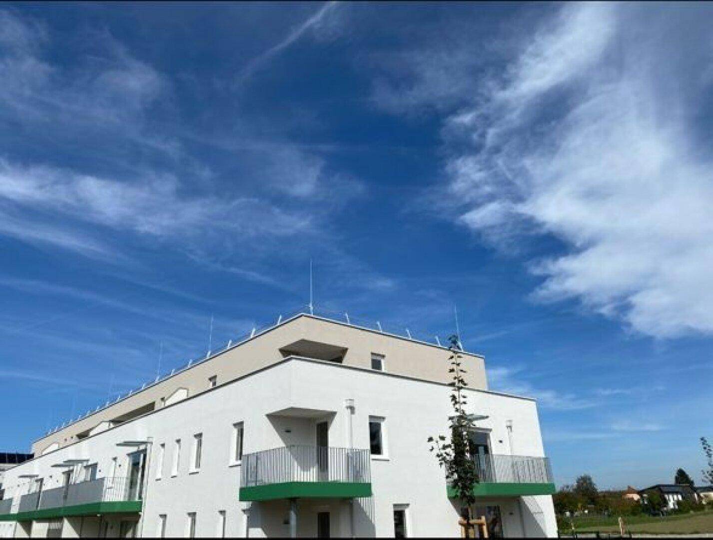 Modernes Gebäude mit weißer Fassade, grünen Balkonen und klarem blauem Himmel.