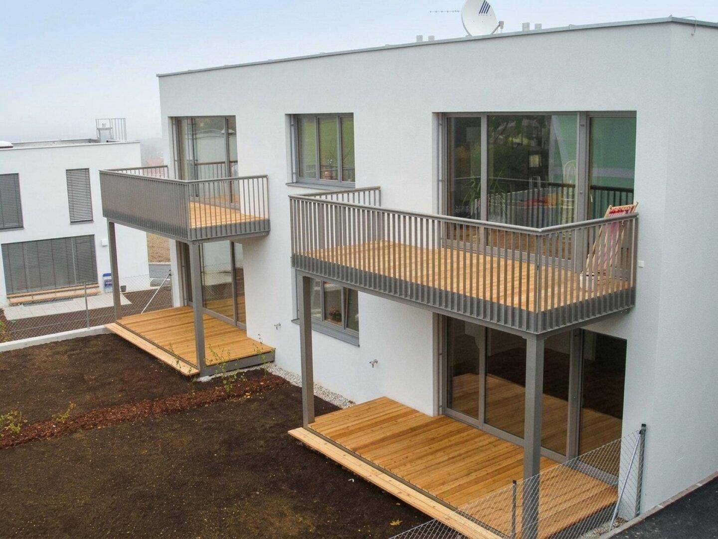 Moderne Balkone und Terrassen mit Holzbelag an einem weißen Neubau mit großen Glasfronten.