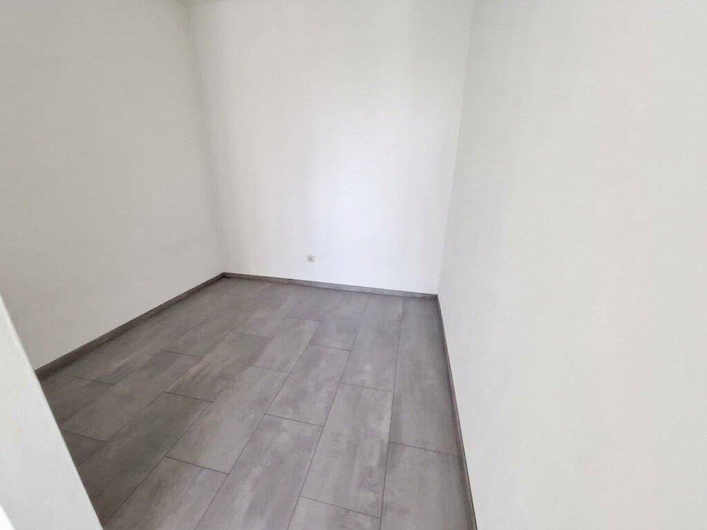 Kleiner, leerer Raum mit weißen Wänden und dunklem Fliesenboden, ideal als Abstellraum.