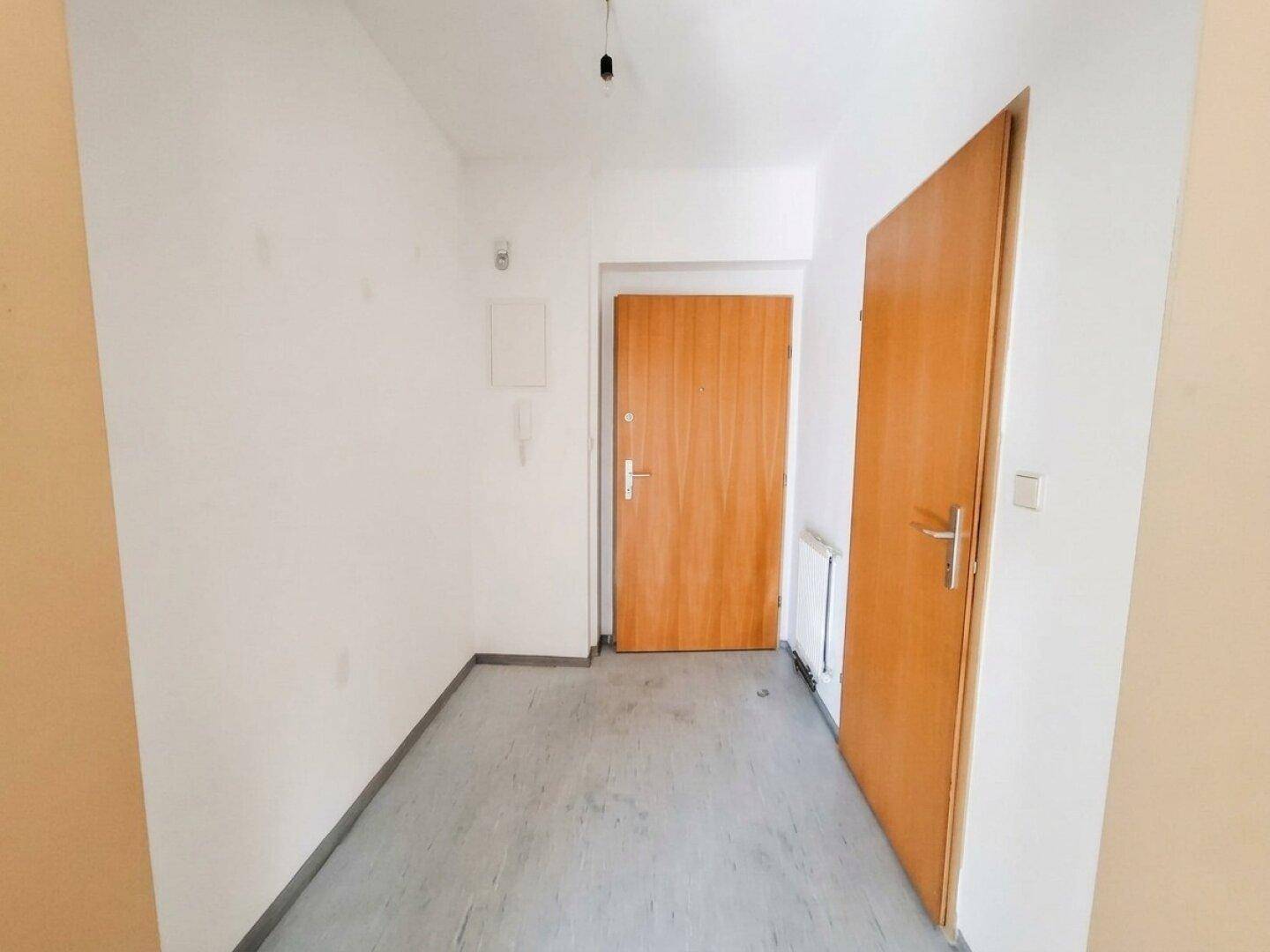 Schlichter Flur mit zwei Holztüren, weißen Wänden und grauem Bodenbelag.