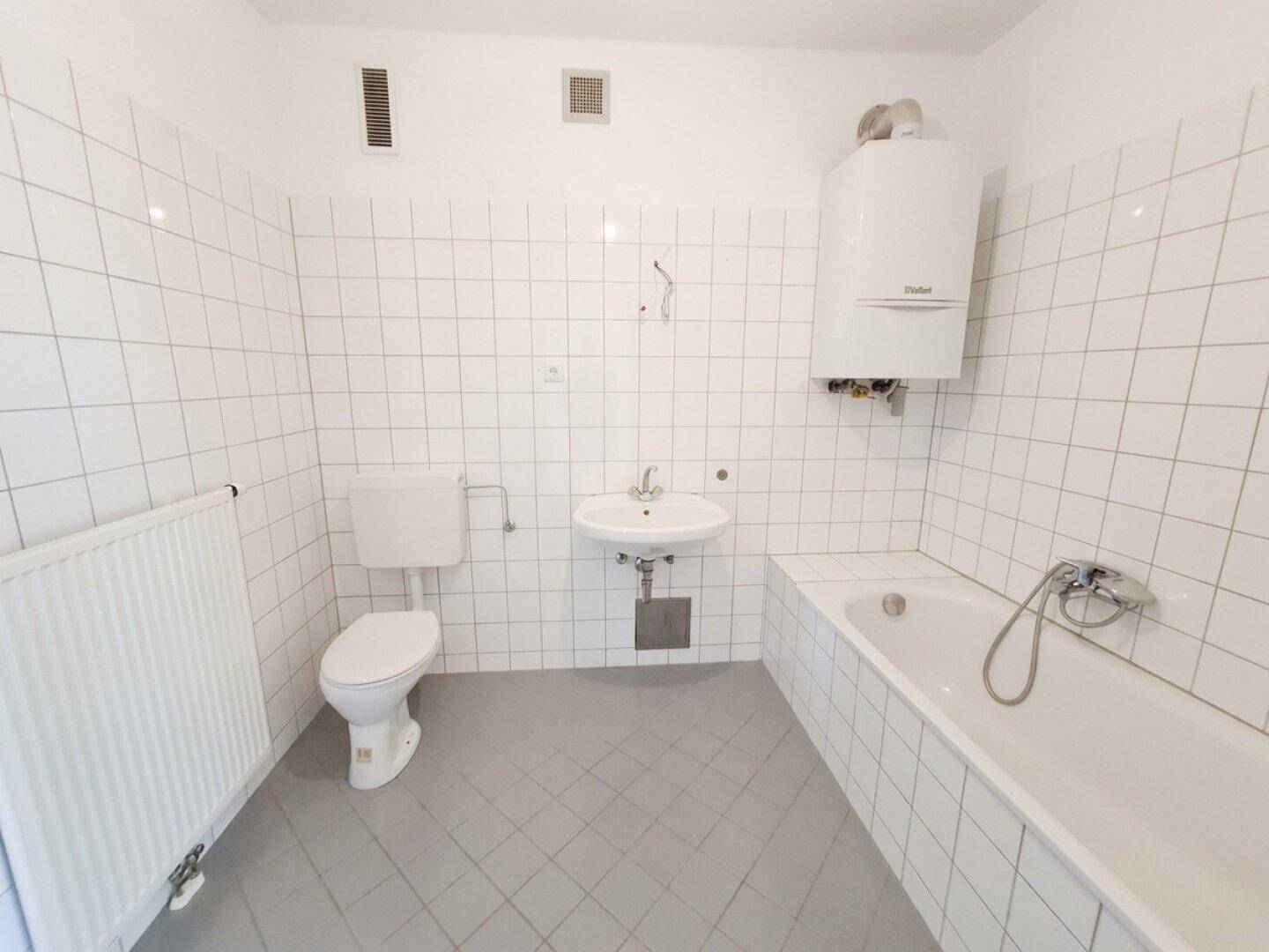 Funktionales Badezimmer mit weißen Fliesen, Badewanne, WC und Warmwasserboiler.