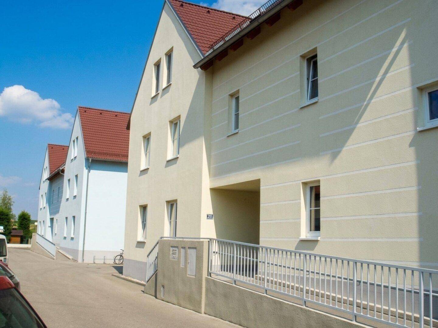 Mehrfamilienhaus mit heller Fassade, rotem Ziegeldach und barrierefreiem Zugang über eine Rampe.