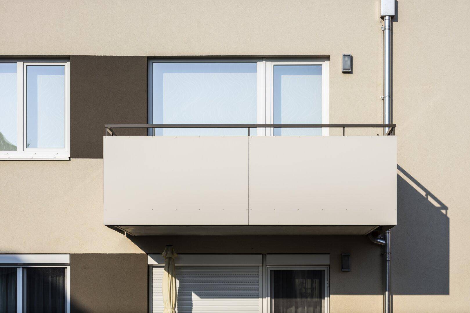 Detailansicht eines modernen Balkons mit schlichtem Geländer und großen Fenstern der Wohnung.