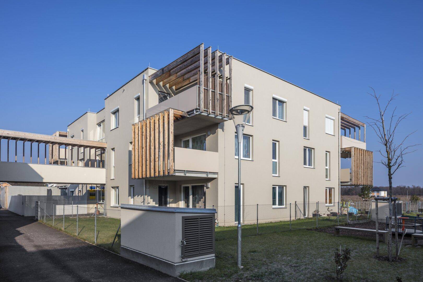 Zeitgenössisches Mehrfamilienhaus mit beiger Fassade, Holzlamellen an den Balkonen und großen Fenstern.