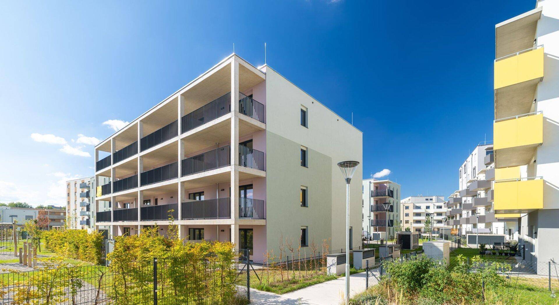 Modernes Mehrfamilienhaus mit Balkonen und gepflegter Grünanlage unter blauem Himmel.