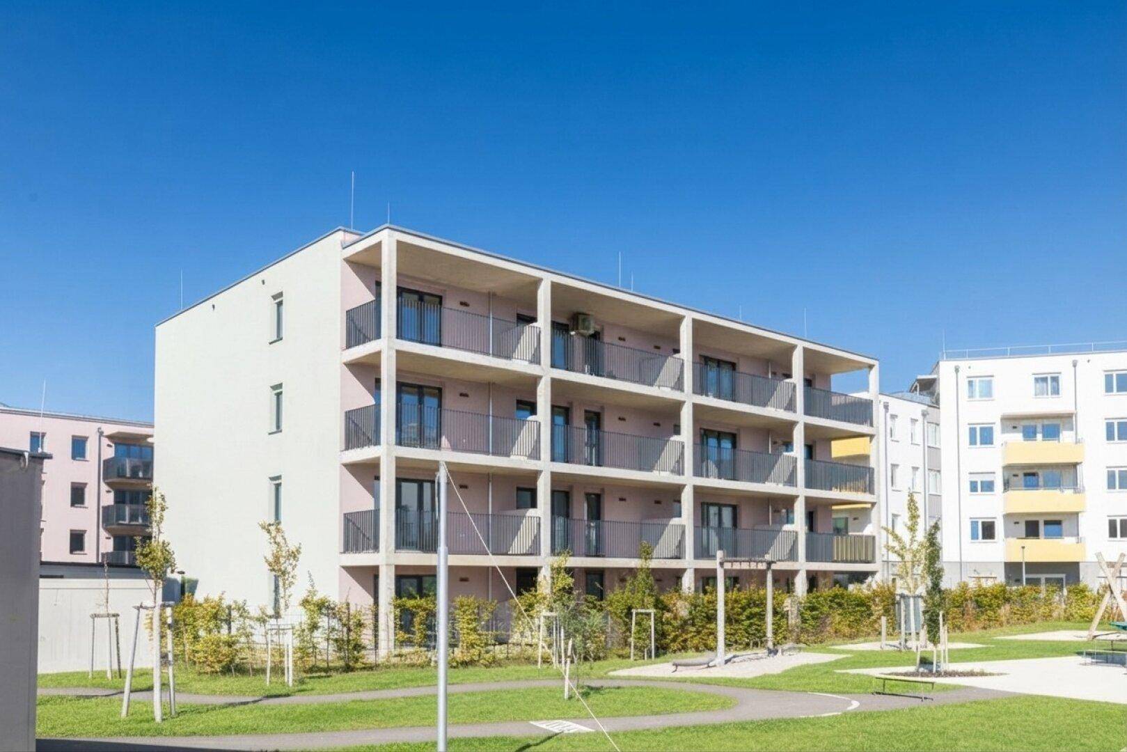 Neubau-Wohngebäude mit mehreren Balkonen und einer weitläufigen Rasenfläche im Vordergrund.