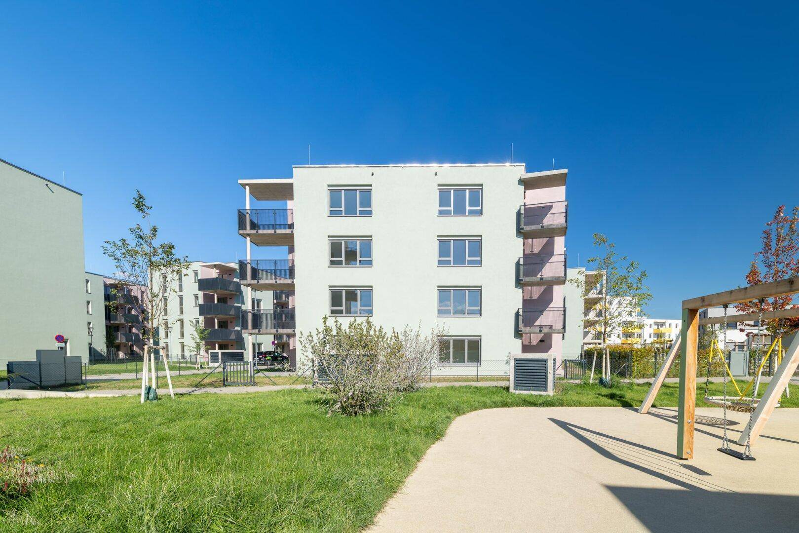 Ansicht eines modernen Wohnhauses mit Spielplatz und Grünflächen in einer neuen Wohnsiedlung.