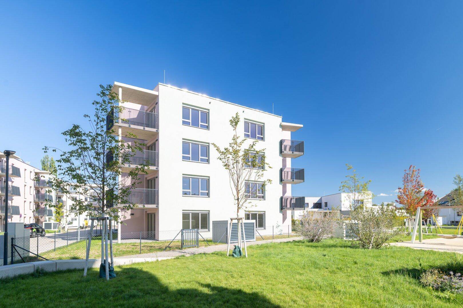 Modernes Wohngebäude mit Balkonen und einem Spielbereich auf einer sonnigen Grünfläche.
