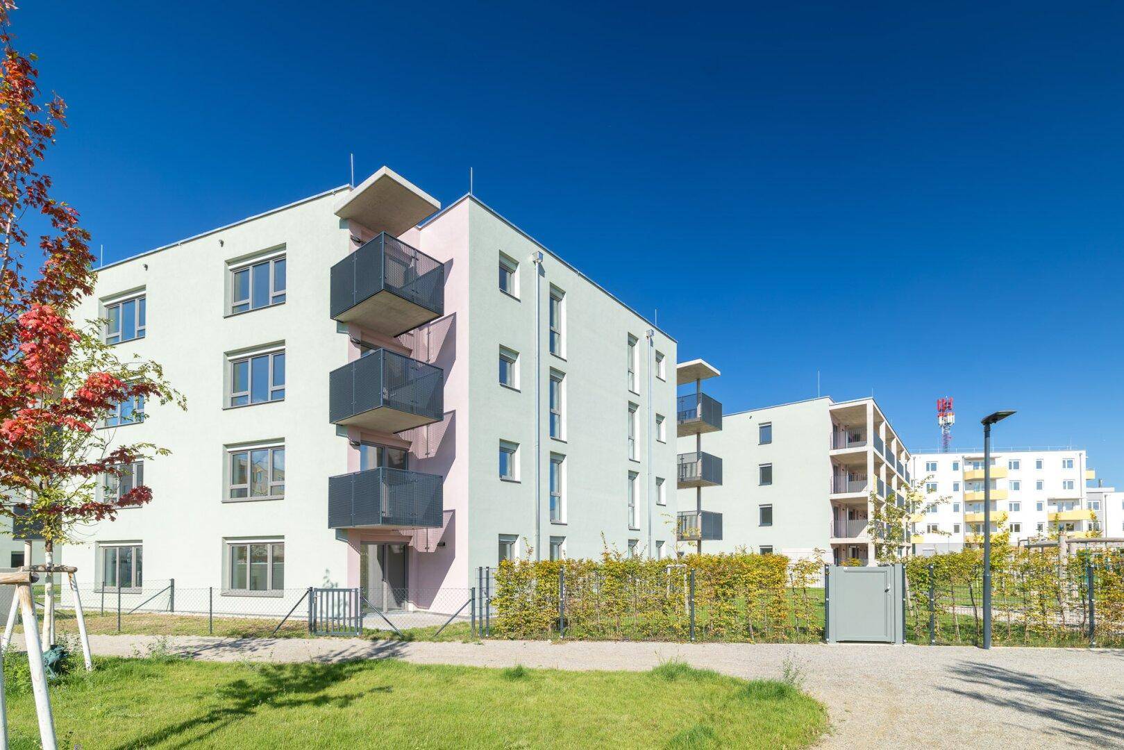 Seitenansicht eines modernen Wohnhauses mit Balkonen und einer Hecke als Grundstücksbegrenzung.
