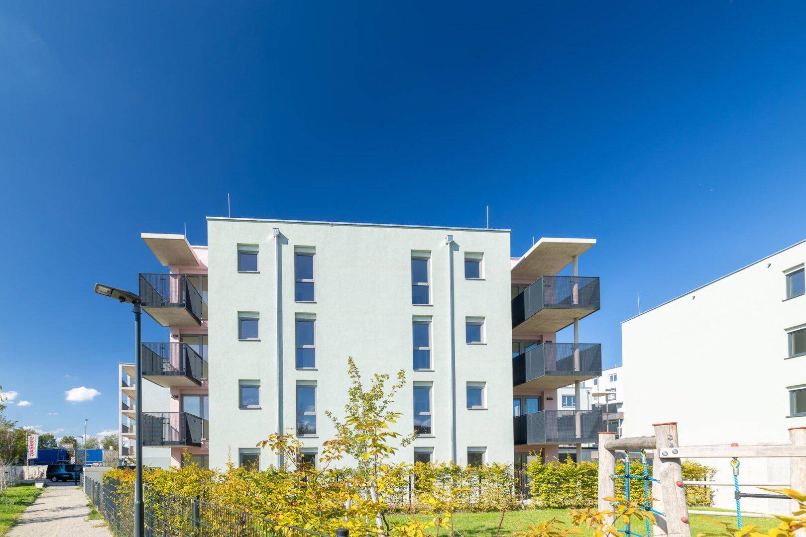Modernes Mehrfamilienhaus mit Balkonen und einem Spielplatz in der gepflegten Außenanlage.