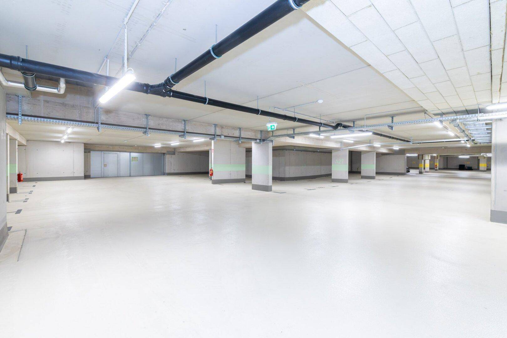 Geräumige und helle Tiefgarage mit sauberem Boden und sichtbaren Installationen an der Decke.